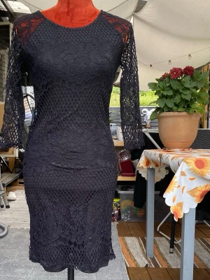 Lindex svart klänning, storlek S - Klänning med långa ärmar och rund halsringning. Klänningen har ett detaljerat spetsmönster över hela plagget, vilket ger en elegant textur. Den är figurnära och slutar vid knäna. 53% bomull 42% polyamid 5% elastan Längd: 93 cm Midja: 43 cm 100% polyester  Inga bilder när den sitter på mig! Katter finns i hemmet!