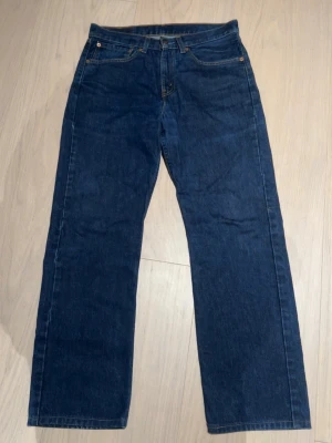 Mörkblå raka jeans från Levi's - Klassiska mörkblå jeans från Levi's med rak passform och fem fickor. Jeansen har synliga sömmar och en läderpatch bak i midjan. 