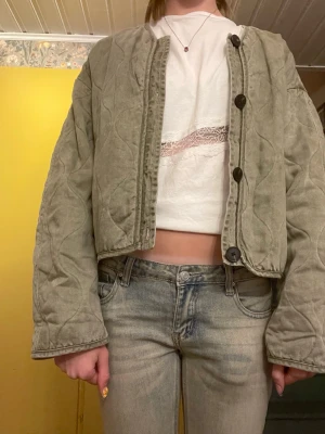 Grön quiltad cardiganjacka - Snygg quiltad cardiganjacka i ljusgrönt med stora svarta knappar framtill. Jackan har en boxy, croppad passform och rundad halsringning. Materialet ser ut att vara mjukt och lite tvättat för en avslappnad look. Perfekt att slänga över en t-shirt för en chill stil.