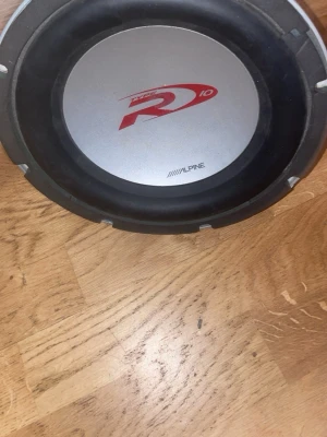 Alpine Type-R 10" subwoofer - Säljer en Alpine Type-R 10-tums subwoofer med silverfärgad front och röd logga. Perfekt för dig som vill ha kraftfull bas i bilen. Rund design med robust material och klassisk Alpine-stil.