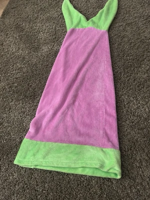 Lila och grön halv onesie mearmaid  - Mysig morgonrock i mjuk frotté med lila kropp och gröna detaljer upptill och nedtill. Modellen har en huva och är perfekt att slänga på sig efter duschen eller när du vill chilla hemma.