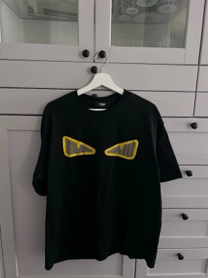Fendi t-shirt  - Cool svart t-shirt från Fendi med ikoniska gula ögon framtill. T-shirten har rund hals och korta ärmar. Tillverkad i mjuk bomull som känns skön mot huden. Perfekt för dig som vill sticka ut med en unik designerstil.
