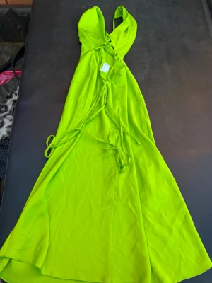 Limegrön långklänning från ASOS DESIGN - Säljer en limegrön långklänning från ASOS DESIGN med snörning framtill och tunna axelband. Klänningen har en figurnära passform upptill och ett svepande fall. Perfekt för sommarens alla tillfällen!