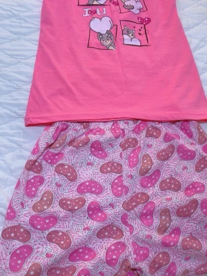 Rosa pyjamas med sött djurmotiv Ny  - Supersöt rosa pyjamas med kortärmad topp och shorts. Toppen har tryck med gulliga djur och texten 'I U'. Shortsen är ljusrosa med mönster av rosa och bruna tofflor samt små hjärtan. Perfekt för mysiga kvällar hemma.