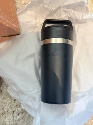 Svart termosmugg från Stanley 354ml - Snygg svart termosmugg från Stanley med matt finish och silverfärgad detalj upptill. Muggen har ett praktiskt handtag på locket och är tillverkad i rostfritt stål. Perfekt för att ta med kaffe eller te på språng.