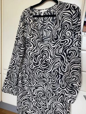 H&M blus mönstrad svart vit stl M - Säljer en stilren svartvit blus från H&M med ett unikt abstrakt mönster. Blusen har långa ärmar och en rund halsringning. Perfekt för att ge din outfit en modern touch. 🖤🤍
