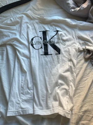 Vit Calvin Klein t-shirt med logga - Snygg vit t-shirt från Calvin Klein Jeans med stor svart CK-logga och text på bröstet. Klassisk passform och rund halsringning. Tillverkad i mjuk bomull som känns skön mot huden. Perfekt till jeans eller shorts.