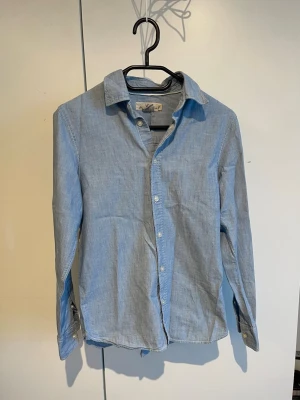 Ljusblå klassisk skjorta - Snygg ljusblå skjorta i bomull med klassisk krage och knäppning framtill. Skjortan har långa ärmar med manschettknappar och en rak passform. Perfekt att styla till jeans eller chinos.