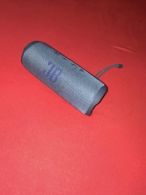 JBL FLIP 6 - Snygg bärbar högtalare i blått med cylinderformad design och tygklädd front. Utrustad med praktisk rem för enkel transport. Perfekt för att ta med sig musiken överallt och har robusta detaljer i plast och tyg.