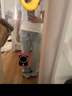 Ljusa baggy jeans med slitningar - Säljer ett par ljusblå baggy jeans med låg midja och slitna detaljer både fram och bak. Jeansen har vida ben och klassiska fickor. Perfekta för en avslappnad och trendig look.