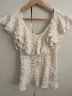 Vit volang topp  - Supersöt vit topp med volangdetaljer runt ringningen. Den är från Lindex i storlek xs. Cremevit