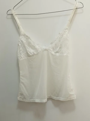 Vit spetstopp babydoll  - Säljer en vit topp med tunna, justerbara axelband och v-ringning. Överdelen har fina spetsdetaljer och resten är i ett mjukt, tunt mesh tyg. Perfekt för dig som gillar en enkel men elegant stil på underkläder, eller som vill ha en vågad partytopp. Se mått på bilder och se gärna mina andra annonser <3 