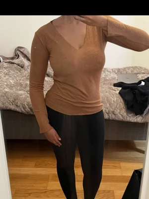 Brun-varm långärmad v-ringad topp. - Snygg brun långärmad topp med v-ringning. Toppen har en slim passform och är tillverkad i ett mjukt material som sitter skönt mot kroppen. Perfekt att styla med jeans eller kjol för en trendig look🌸🌸