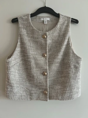 Väst i tweed look - Jättesnygg fin väst med tweed look.   Har aldrig använt den. Hängt i garderoben bara.   Längd: ca 44 cm