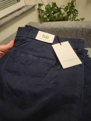 Mörkblå chinos från These Glory Days - Snygga mörkblå chinos från These Glory Days i storlek 56. Klassisk rak passform med bälteshällor, sidofickor och bakficka. Tillverkade i ett mjukt och slitstarkt bomullstyg som ger en clean och stilren look.