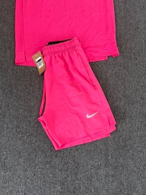  Nike träningsset - Snygga och sportiga rosa träningsshorts från Nike med elastisk midja och vit logga på benet. Perfekta för sommarens alla aktiviteter och har en loose passform för maximal rörelsefrihet.