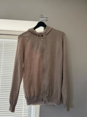 Gran Sasso Kashmir tröja  - En stilren beige hoodie med dragkedja framtill och huva med dragsko. Tröjan har långa ärmar och ribbade muddar vid ärmslut och nederkant. Perfekt för en avslappnad och enkel look.