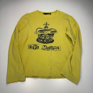 Gul långärmad topp Love Moschino - Cool gul långärmad topp från Love Moschino med svart tryck av krona och text på bröstet. Tillverkad i mjuk bomull med normal passform. Perfekt för dig som vill sticka ut med en statement-piece.0142