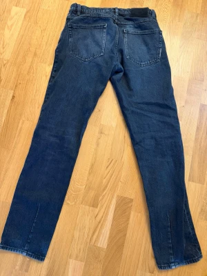 Mörkblå raka jeans - Säljer ett par mörkblå jeans med raka ben och klassisk femficksdesign. Jeansen har bälteshällor och en svart patch bak i midjan. Materialet är denim i bomull och passformen är avslappnad men ändå smal. W30 L34