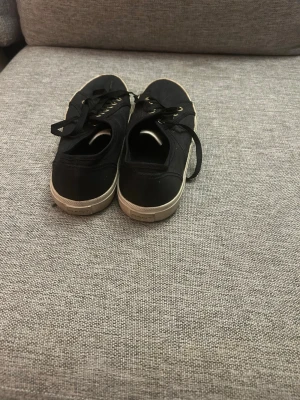 Svarta låga sneakers från Gant - Snygga svarta sneakers från Gant med vita sulor och svarta skosnören. Skorna har guldfärgade detaljer vid snörningen och är tillverkade i canvasmaterial. Perfekta för en avslappnad och trendig stil.