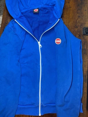 Blå Colmar zip-hoodie - Snygg blå hoodie från Colmar med vit dragkedja och huva. Klassisk Colmar-logga på armen. Perfekt för en avslappnad och sportig stil. Tillverkad i mjukt material som känns skönt mot huden.