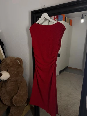 Röd långklänning - Snygg röd långklänning med rynkade detaljer på sidan. Klänningen har en enkel, ärmlös design och en rak passform som ger en stilren look. Perfekt för dig som vill sticka ut med en klassisk färg och elegant siluett. Aldrig använd utan prislapp 