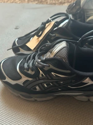 Svarta och silver sneakers - Snygga sneakers i svart och silver med meshdetaljer och coola mönster längs sidorna. Skorna har en sportig vibe med tjock sula och snörning. Perfekta för dig som gillar streetstyle och vill sticka ut.