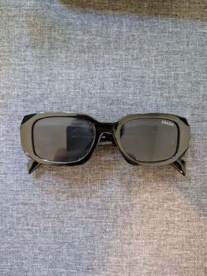 Prada solglasögon svarta - med box - Prada solglasögon i svart, kantig design med fasetterade skalmar. Gott skick. Kommer med originalbox och häfte. Prissatt lågt för snabb affär.
