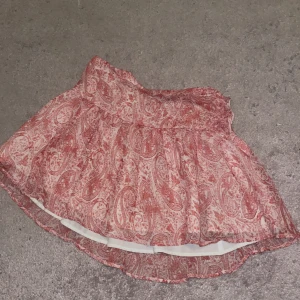 Rosa vit mönstrad kjol från Gina Tricot - Supersöt röd och vit kjol från Gina Tricot med paisleyinspirerat mönster. Kjolen är kort och har en lätt utställd form med volangkant nertill. Perfekt för dig som gillar färg och mönster!