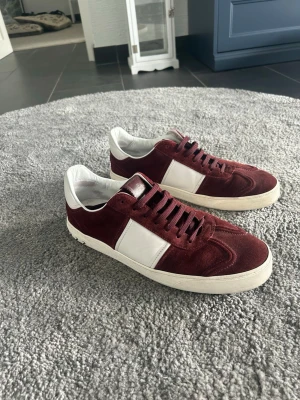 Valentino flycrew vinröda  - Snygga sneakers i vinrött mocka med vita läderdetaljer och vit sula. Skorna har lågt skaft och coola nitar på hälen för extra edge. Perfekta för dig som vill sticka ut med stilrena men unika sneakers.