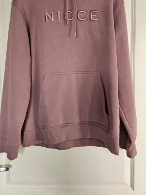 Ljuslila hoodie från NICCE herr storl.L - Säljer en ljuslila hoodie från NICCE med broderad logga på bröstet. Hoodien har en stor känguruficka framtill, dragsko i huvan och ribbade muddar. Materialet känns mjukt och skönt, perfekt för chill dagar.