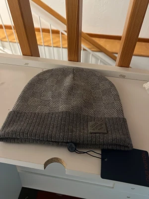 Grå mössa från hm - Snygg grå mössa från hm med diskret rutmönster och ribbad kant. Märkeslapp framtill och klassisk passform. Perfekt accessoar för att hålla värmen med stil.
