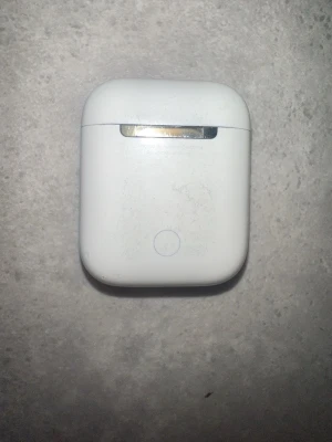 Used Apple AirPods (1st or 2nd Gen) with Charging Case - This is a pair of Apple AirPods (either 1st or 2nd generation) with their original charging case. The case and earbuds show visible signs of wear, including dirt and scuff marks, especially around the lid and the inside where the earbuds sit. The case has a pairing button on the back, which is typical for these generations. The AirPods themselves appear intact but may need cleaning.
