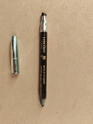 Svart ögonbrynspenna från Lancôme - Snygg svart ögonbrynspenna från Lancôme med metalliskt lock. Pennan har en snedställd spets för enkel applicering och är perfekt för att forma och fylla i brynen. Klassisk design med guldtext och detaljer.