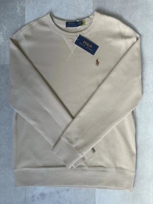 Polo Ralph Lauren Tröja  - Stilren beige sweatshirt från Polo Ralph Lauren med klassisk rund halsringning och broderad logga på bröstet. Perfekt för en clean och avslappnad look. Den är helt ny och är otroligt skön. 