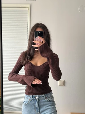 Brun ribbad långärmad topp - Snygg brun ribbad topp med v-ringning och långa ärmar. Figurnära passform och stretchigt material som sitter bekvämt. Perfekt att styla med jeans eller kjol för en trendig look.