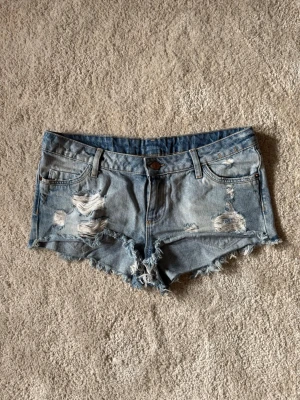 Blå slitna jeansshorts med fransar - Säljer ett par ljusblå jeansshorts med slitna detaljer och fransig kant. 
