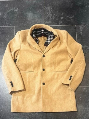 Elegat Beige Herrkappa / Ullrock med Löstagbar Halsduk - Stilren och välskräddad beige herrkappa i skön ullblandning. Kappan är helfodrad med ett stickat och vadderat innerfoder som håller värmen bra under höst och vinter.