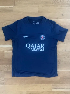 Mörkblå PSG matchtröja från Nike - Snygg mörkblå PSG matchtröja från Nike med klubbmärke och Qatar Airways-tryck på bröstet. Tröjan har rund hals, korta ärmar och är tillverkad i ett lätt och funktionellt material som passar perfekt till fotbollsträning eller match.