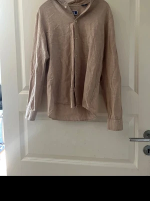Beige linneskjorta från Jack & Jones - Säljer en stilren beige skjorta från Jack & Jones i luftigt linne. Skjortan har klassisk krage, knappar framtill och långa ärmar. Perfekt för dig som gillar en avslappnad men snygg look.