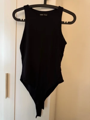 Svart body från SHEIN, storlek S - En enkel och stilren svart body från SHEIN i storlek S. Bodyn har breda axelband, rund halsringning och är tillverkad i ett mjukt, stretchigt material som sitter tajt mot kroppen. Perfekt att matcha med jeans eller kjol för en clean look.