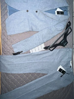Ljusblå kostym från Jack & Jones - Snygg ljusblå kostym från Jack & Jones i linneblandning. Kavajen har två knappar och klassisk krage, matchande byxor med pressveck. Perfekt för dig som vill ha en stilren och modern look.