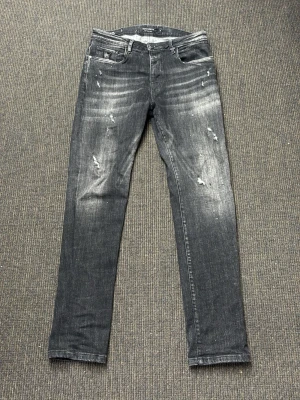Svarta slitna jeans - Säljer ett par svarta jeans med slitningar och tvättade detaljer. Jeansen har fem fickor och en klassisk knappgylf. Materialet är denim med stretch för skön passform. Perfekta för en avslappnad och trendig look. Knappt använda i mycket gott skick!