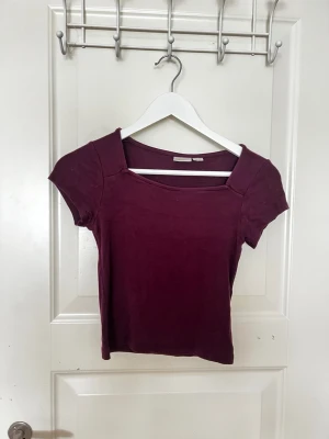 Mörklila topp från Gina Tricot - Snygg mörklila topp från Gina Tricot med korta ärmar och fyrkantig ringning. Toppen är croppad och har en enkel, stilren design som passar perfekt till jeans eller kjol. Tillverkad i mjukt material för skön känsla.
