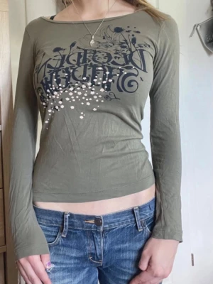 Olivgrön långärmad topp med tryck - Snygg olivgrön boatneck långärmad topp med svart tryck och vita detaljer framtill. Perfekt till jeans eller liknande nu till hösten! 