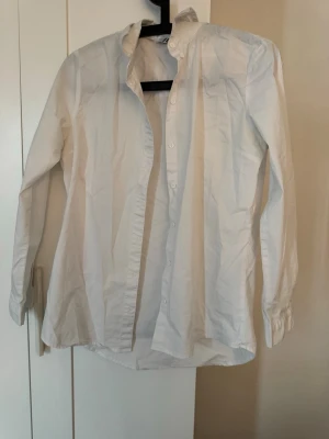 Vit skjorta från JDY med knappar - Klassisk vit skjorta från JDY i storlek 36. Skjortan har långa ärmar, knappar framtill och en enkel, stilren design. Perfekt att styla till olika outfits och tillfällen. Tillverkad i mjuk bomull för en bekväm känsla.