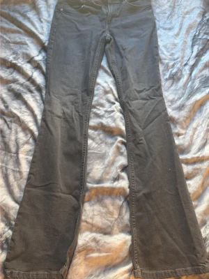 Mörk gråa bootcut jeans - Säljer ett par mörk gråa bootcut jeans med klassisk femficksmodell. Jeansen har utsvängda ben och normal midja. Materialet är mjukt denim som ger en skön passform och en avslappnad look. Perfekta för dig som gillar retrovibbar och vill ha ett par jeans som sticker ut.