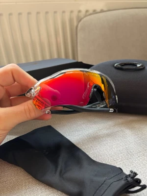 Oakley Radar EV  - Säljer ett par original Oakley Radar EV Path med Prizm Road-lins. Glasögonen är lätta, bekväma och passar perfekt för golf, cykling, löpning och annan träning. Säljs komplett med original Oakley-fodral och mjuk förvaringspåse.  Glasögonen är i fint bruksskick med normala tecken på användning. Linsen har mindre kosmetiska märken men inga skador som påverkar funktionen eller sikten. Ett riktigt bra val för dig som vill ha ett par högkvalitativa sportglasögon till ett bra pris.