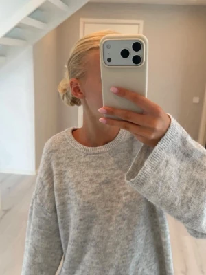 Ljusgrå oversized stickad tröja - Mysig ljusgrå stickad tröja med oversized passform och rund halsringning. Tröjan har långa ärmar och är tillverkad i ett mjukt material som passar perfekt för kyligare dagar. Enkel och stilren design som är lätt att matcha.