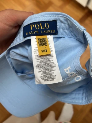 keps från Polo Ralph Lauren - Snygg ljusblå keps från Polo Ralph Lauren med klassisk böjd skärm och broderad Polo-logga på sidan. Tillverkad i mjuk bomull som andas. Perfekt accessoar för en avslappnad och stilren look. Andvänd fåtal gånger.